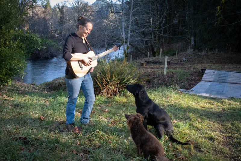 Grisha with labrador and poodle cocker spaniel mix at a river. Grisha is holding a guitar. Both dogs looking at Grisha